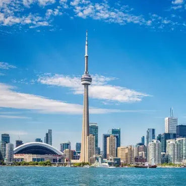 esim data Canada Premium visit Toronto skyline with the CN Tower standing prominently in the center, surrounded by modern high-rise buildings under a bright blue sky with scattered white clouds, with water in the foreground.