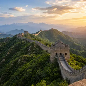 The Great Wall of China winding along green mountain ridges under a warm sunset sky with soft clouds.
