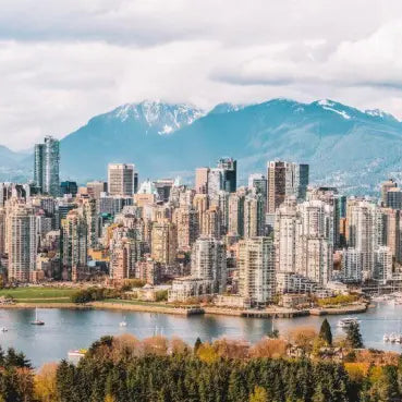 esim data trip Canada unlimited use visiting Panoramic view of the Vancouver skyline with modern high-rise buildings, a harbor in the foreground, and snow-capped mountains under a cloudy sky.